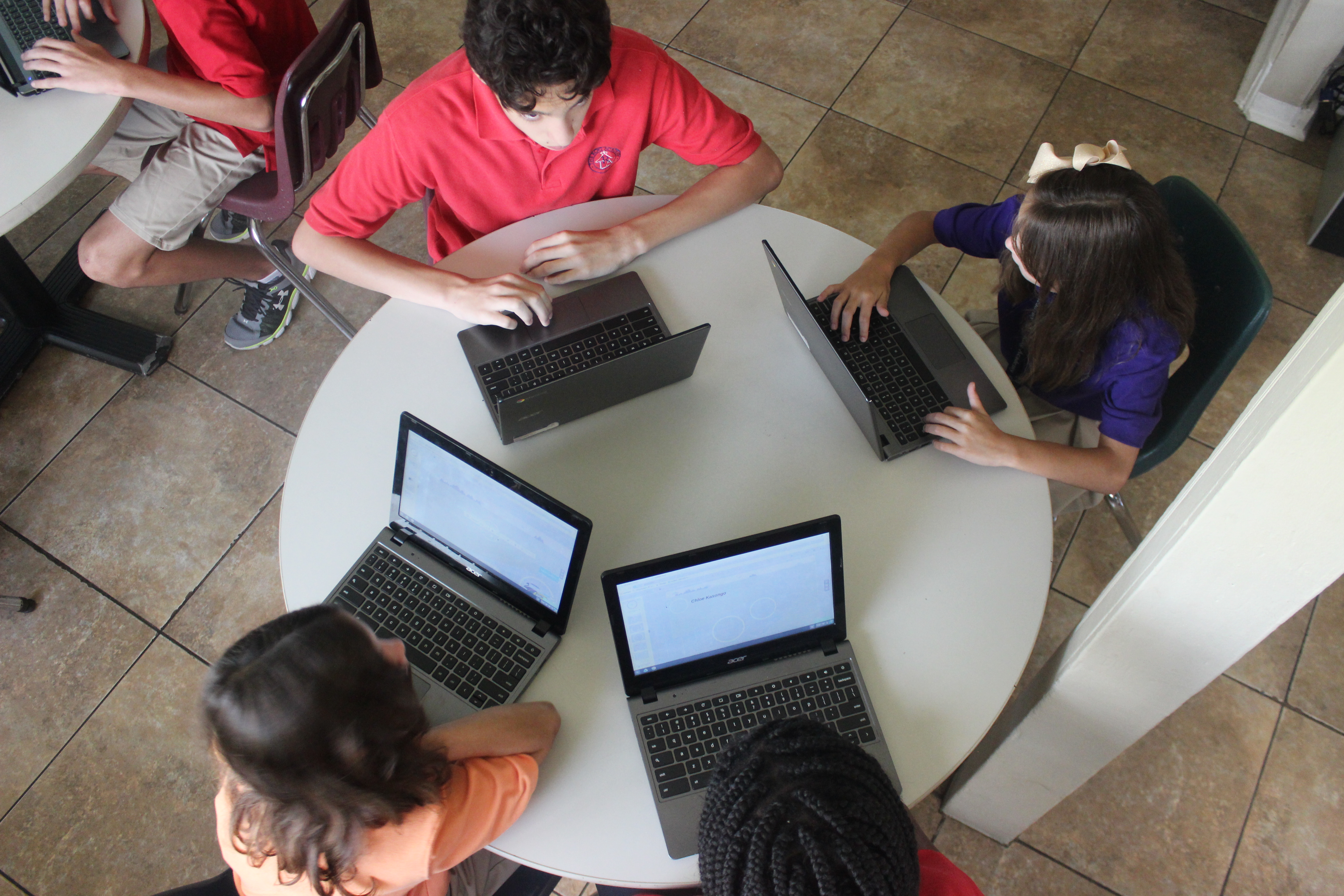 4 kids sitting around a table using laptops