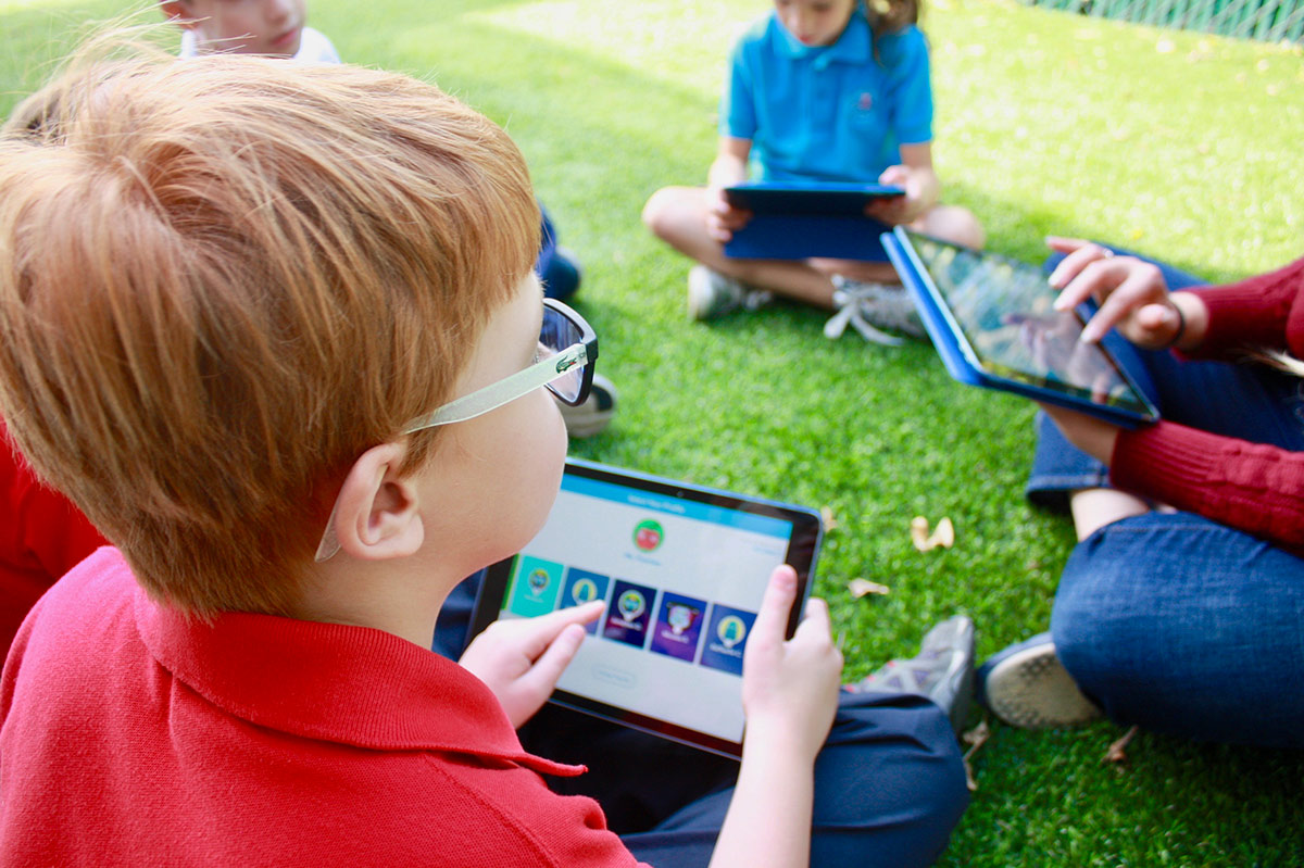 4 kids sitting in a circle outside using ipads