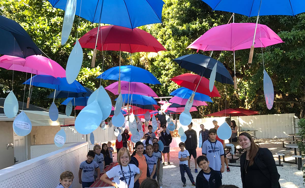 children standing outside picnic tables with colorful umbrellas above them